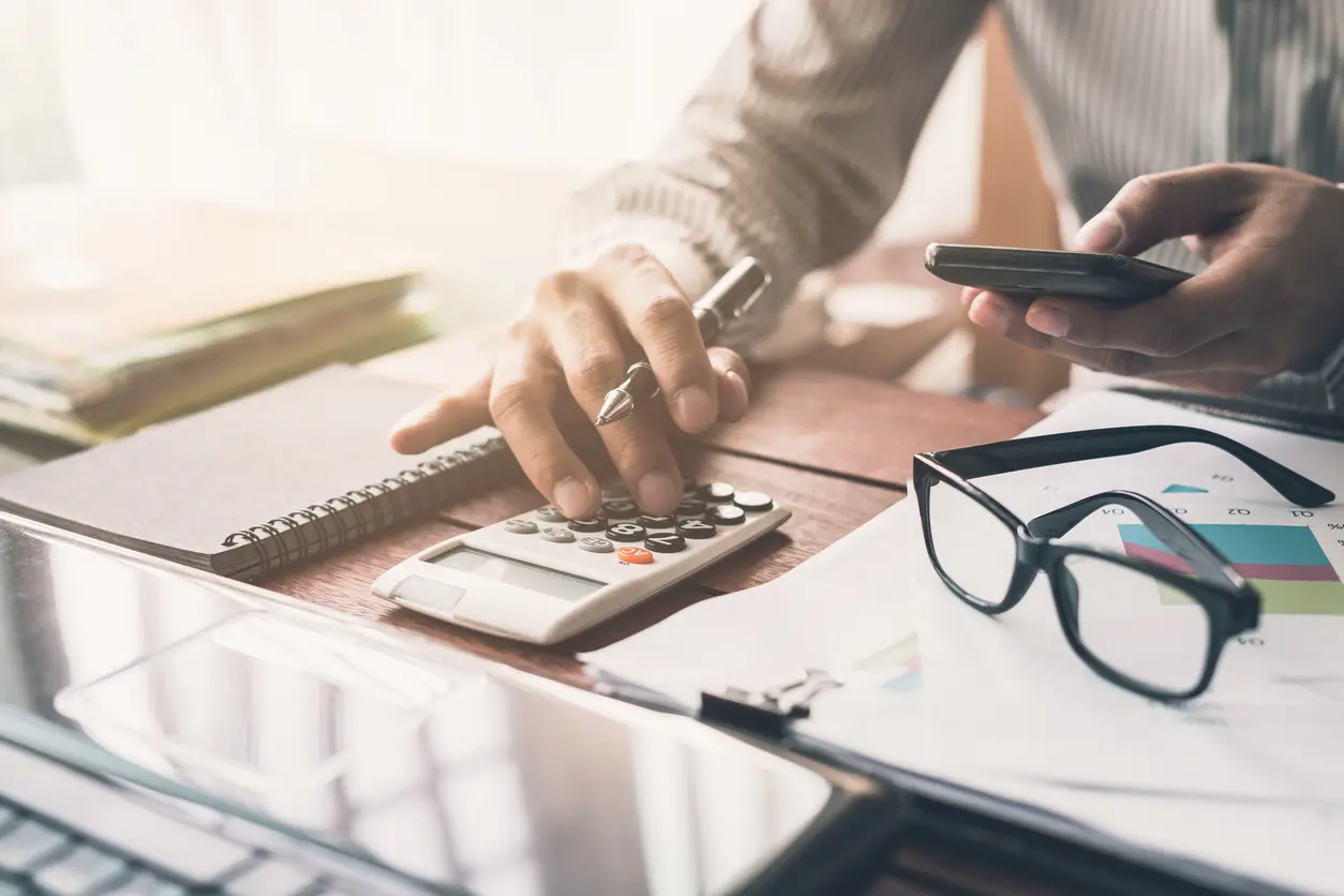 Mãos fazendo cálculos em uma calculadora sobre a mesa de trabalho